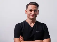 Portret mężczyzny w czarnym scrubie medycznym, ze skrzyżowanymi rękami.