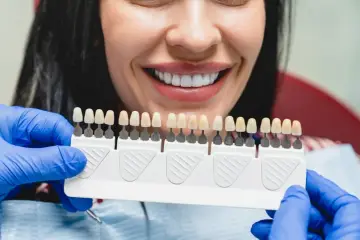 Uśmiechnięta kobieta z idealnymi zębami, dentysta dobiera kolor licówek. Sprawdź, jaka jest licówki cena.