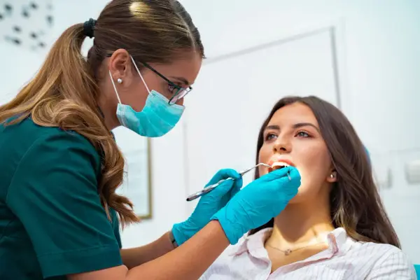 Dentystka w masce i rękawiczkach bada zęby pacjentki. To nie jest wyrywanie 8, ale rutynowa kontrola.